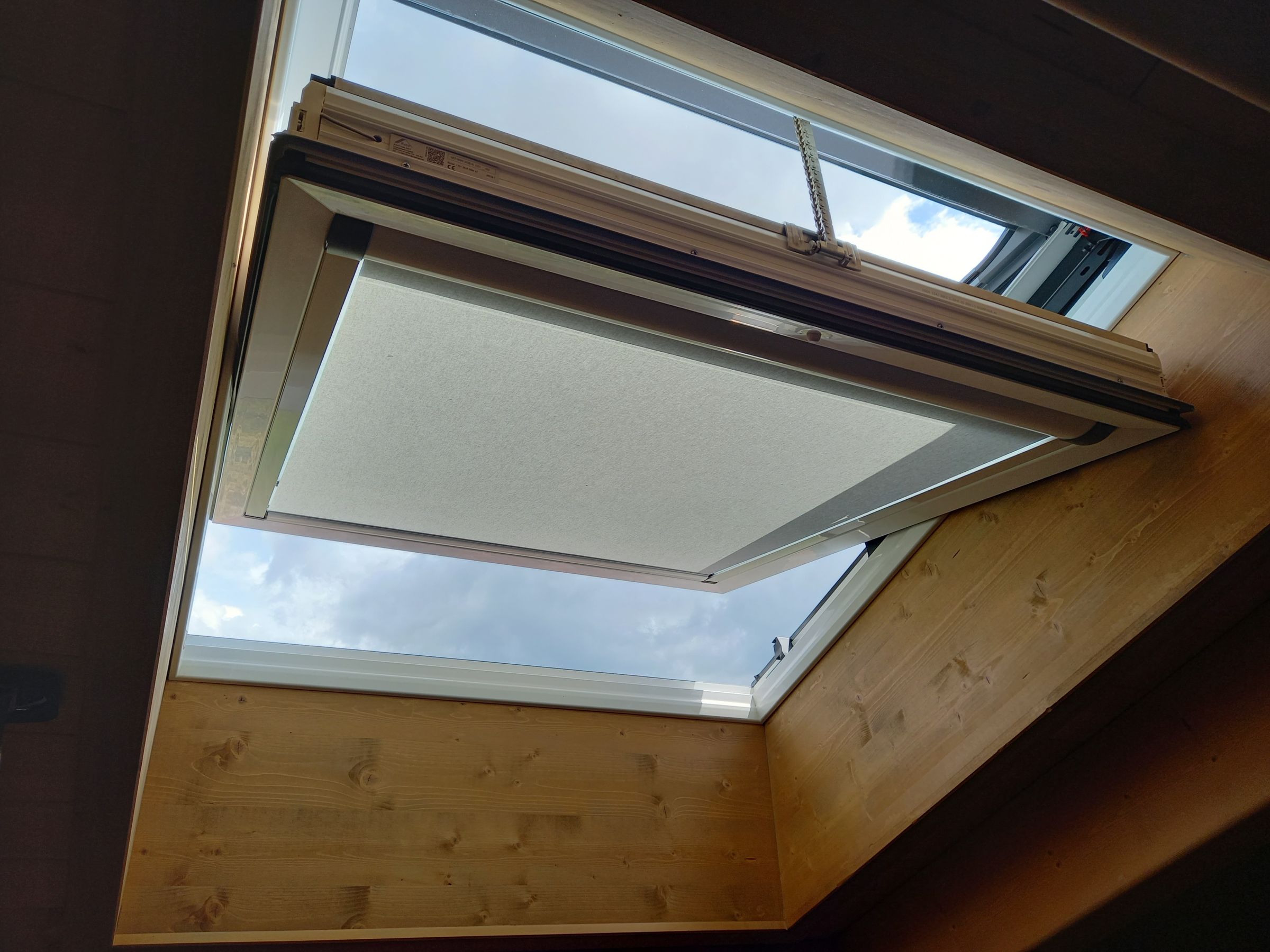 Finestra per tetti ROTO elettrica con tenda, vista dall’interno di una mansarda in legno
