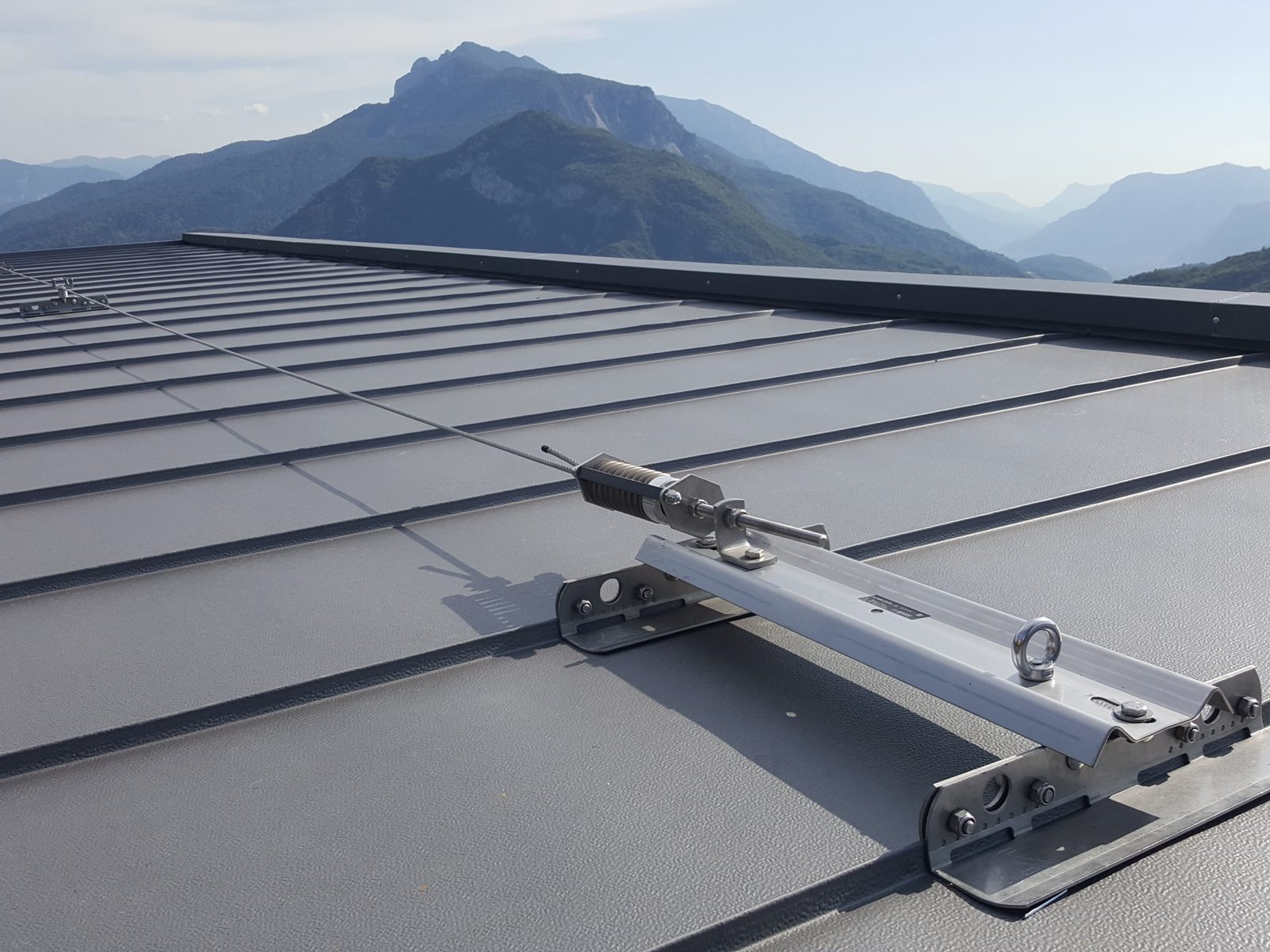 Tenditore della linea vita all’estremità della copertura, con le montagne del Trentino sullo sfondo